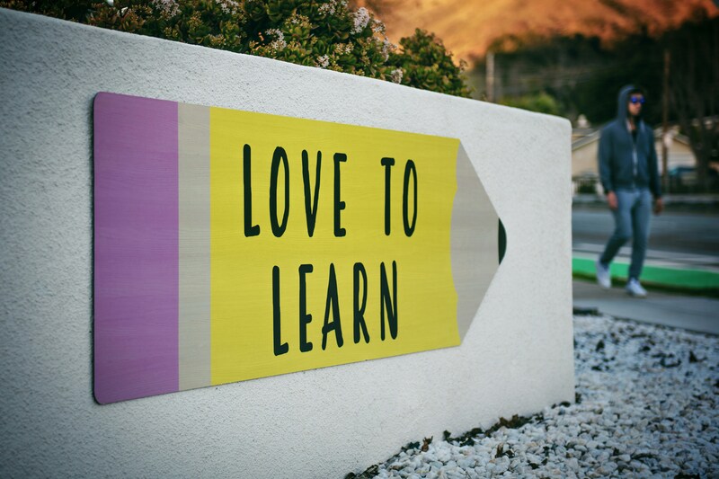 Une pancarte blanche avec un crayon jaune avec la base gomme de couleur rose où est écrit "love to learn"